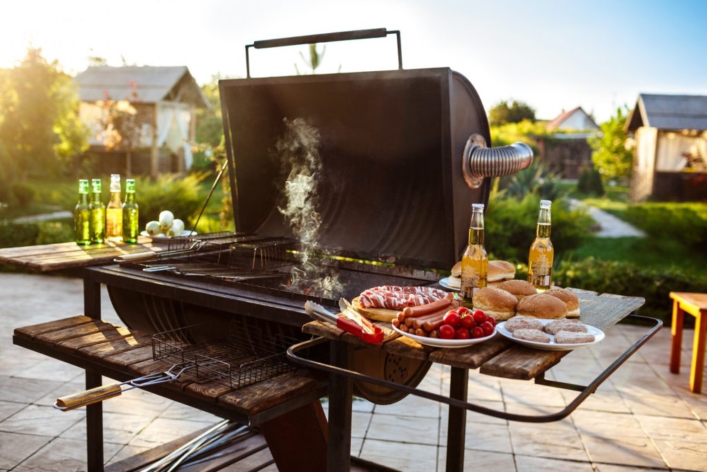 Fatgrill med öppet lock och grillmat på ett bord i en solig trädgård