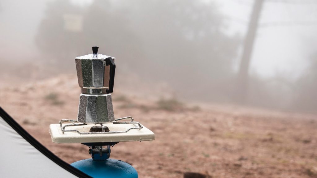 Liten gasolbrännare med kaffebryggare på en blå gasolbehållare utomhus