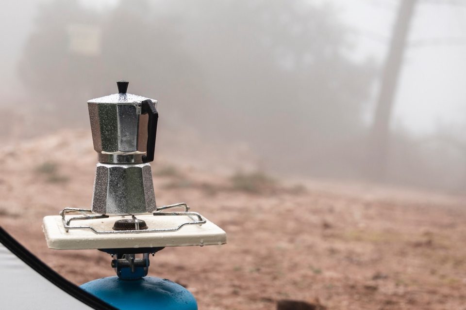 Liten gasolbrännare med kaffebryggare på en blå gasolbehållare utomhus